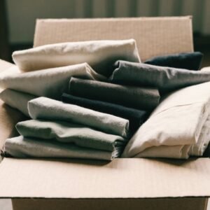 Folded assorted clothing in neutral tones inside an open carton