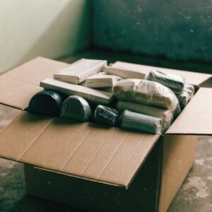 An opened carton of assorted goods in plain packaging on a concrete floor